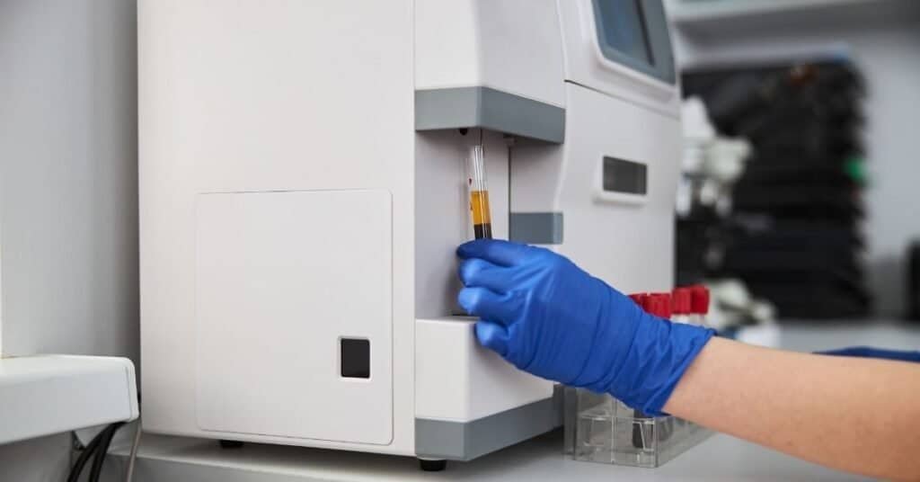 A laboratory technician placing blood samples into a hematology analyzer machine for comprehensive blood analysis.